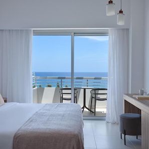 A hotel room with a bed, a small table, a chair, a bench, and a view of the ocean. - Atlantica Sea Breeze - Adults Only (Paralimni)