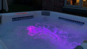 Un jacuzzi con iluminación morada, una casa de ladrillo y una ventana.