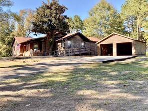 A rustic cabin with a porch, a garage, and a large tree in front. - Noccalula Mountain Retreat-The ByrdHouse (Gadsden)