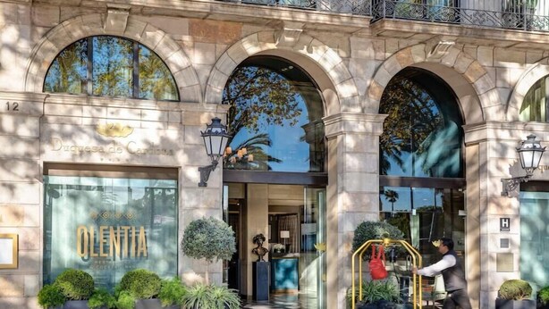 A hotel entrance with a large glass facade, a sign reading "OLENTIA," and a man pushing a cart. - Duquesa de Cardona (Barcelona)