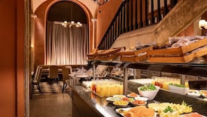 A buffet with various food items, including fruits, vegetables, and pastries, in a room with a checkered floor and a staircase in the background. - Duquesa de Cardona (Barcelona)