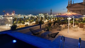 A rooftop pool area with lounge chairs and umbrellas, overlooking a cityscape with a bridge and buildings. - Duquesa de Cardona (Barcelona)