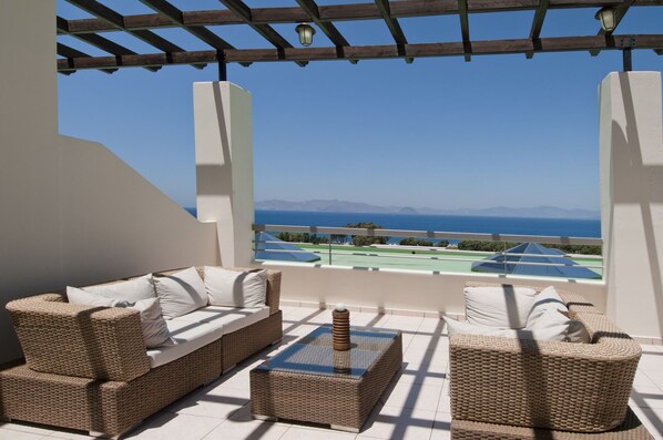 Un balcon avec des meubles en osier, une vue sur la mer et un court de tennis.
