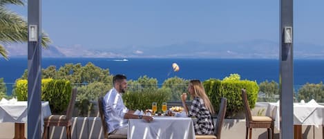 Una pareja cenando en una mesa con vistas al mar y a las montañas.