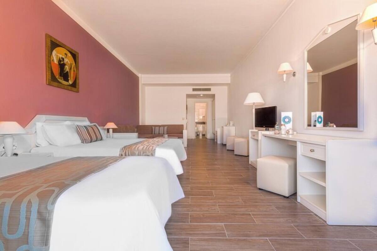 Een hotelkamer met een groot bed, een bureau met spiegel, een televisie en een badkamer in de achtergrond.