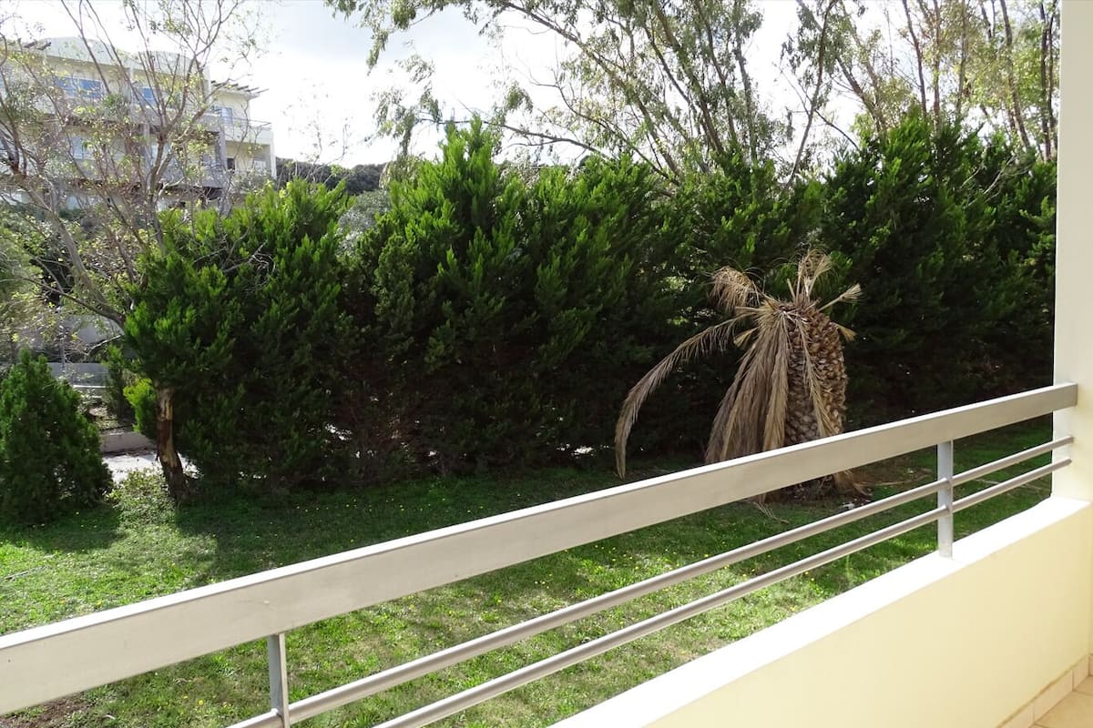 A balcony with a metal railing, a palm tree, and dense green shrubbery.
