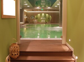 Zona de piscina con escalones que la conducen, rodeada de muros verdes y un techo con iluminación empotrada.