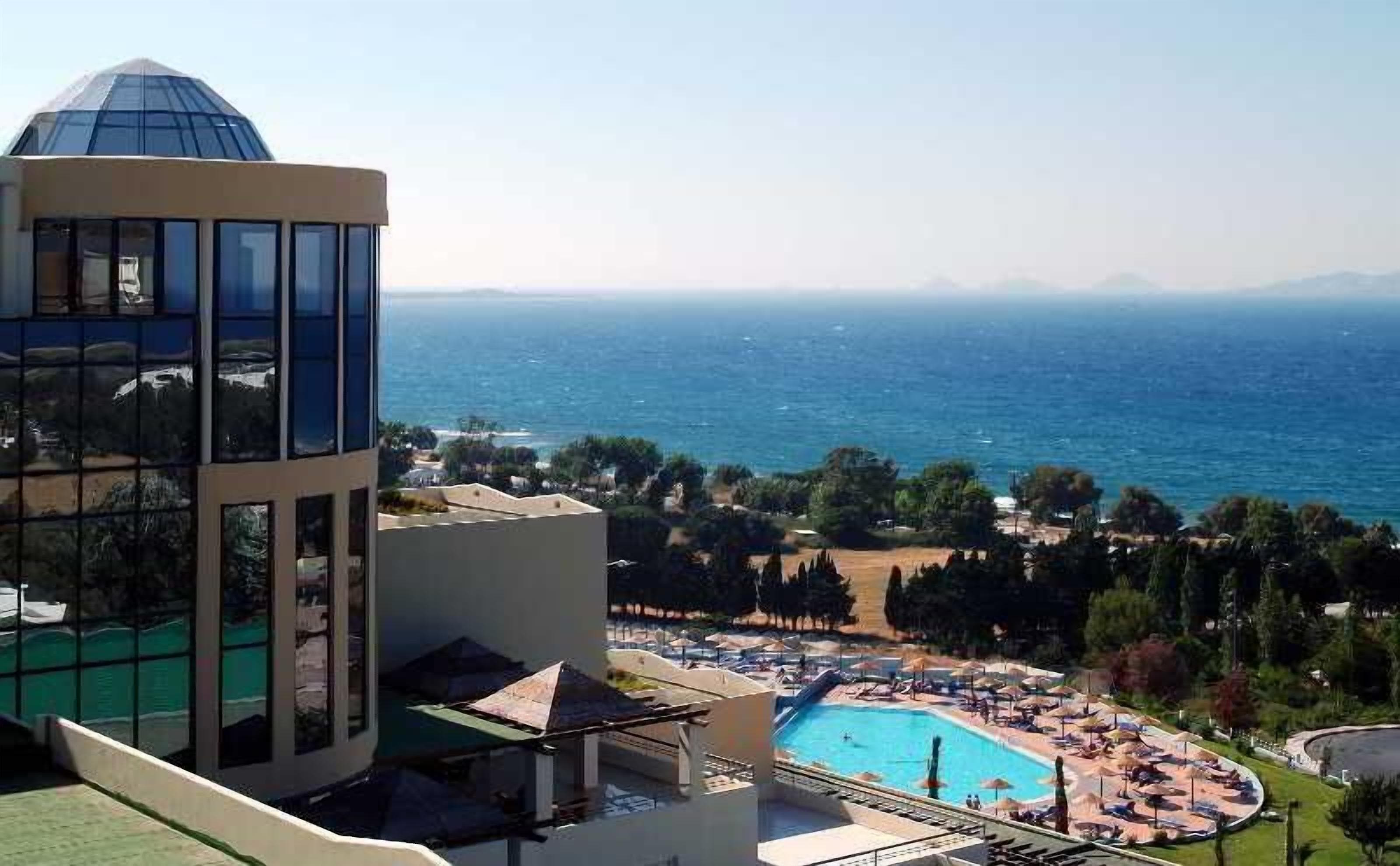 A hotel with a pool, a view of the sea, and a mountainous landscape in the background.