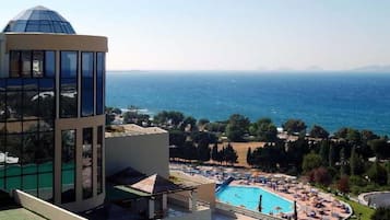 A hotel with a pool, a view of the sea, and a mountainous landscape in the background.