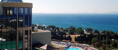 A hotel with a pool, a view of the sea, and a mountainous landscape in the background.