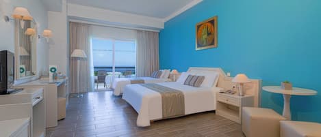 A hotel room with two beds, a desk, a chair, a TV, and a view of the sea.