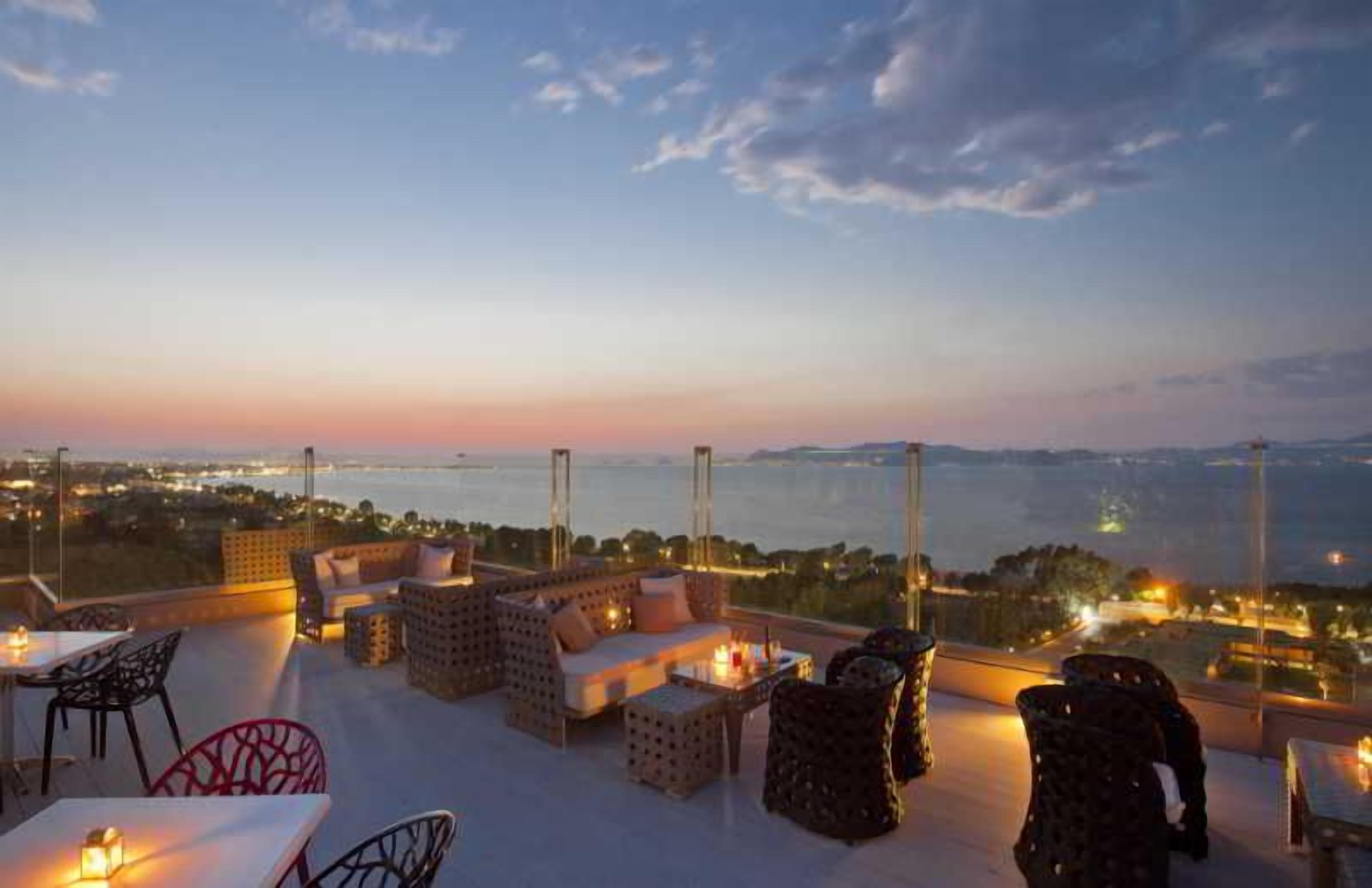 A rooftop terrace with outdoor seating, a view of the city, and a sunset.