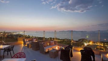 A rooftop terrace with outdoor seating, a view of the city, and a sunset.