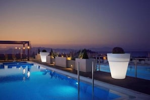 A swimming pool with lounge chairs and planters, set against a twilight sky. - Kipriotis Panorama and Suites (Kos)