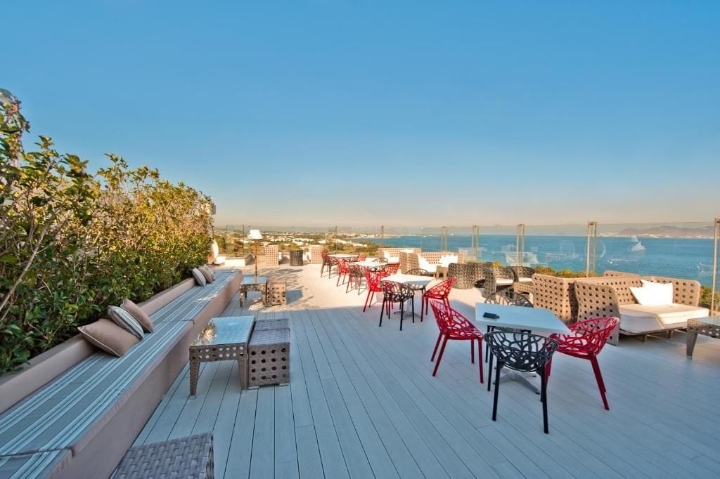 A rooftop terrace with seating and tables, overlooking a coastal cityscape.
