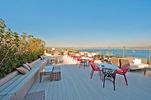 A rooftop terrace with seating and tables, overlooking a coastal cityscape.