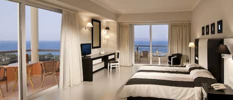 Una camera d'hotel moderna con un letto grande, una scrivania, una TV e un balcone con vista sul mare.