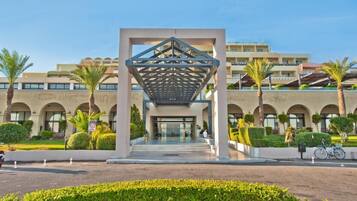 A modern hotel entrance with a geometric canopy, arched windows, and palm trees.
