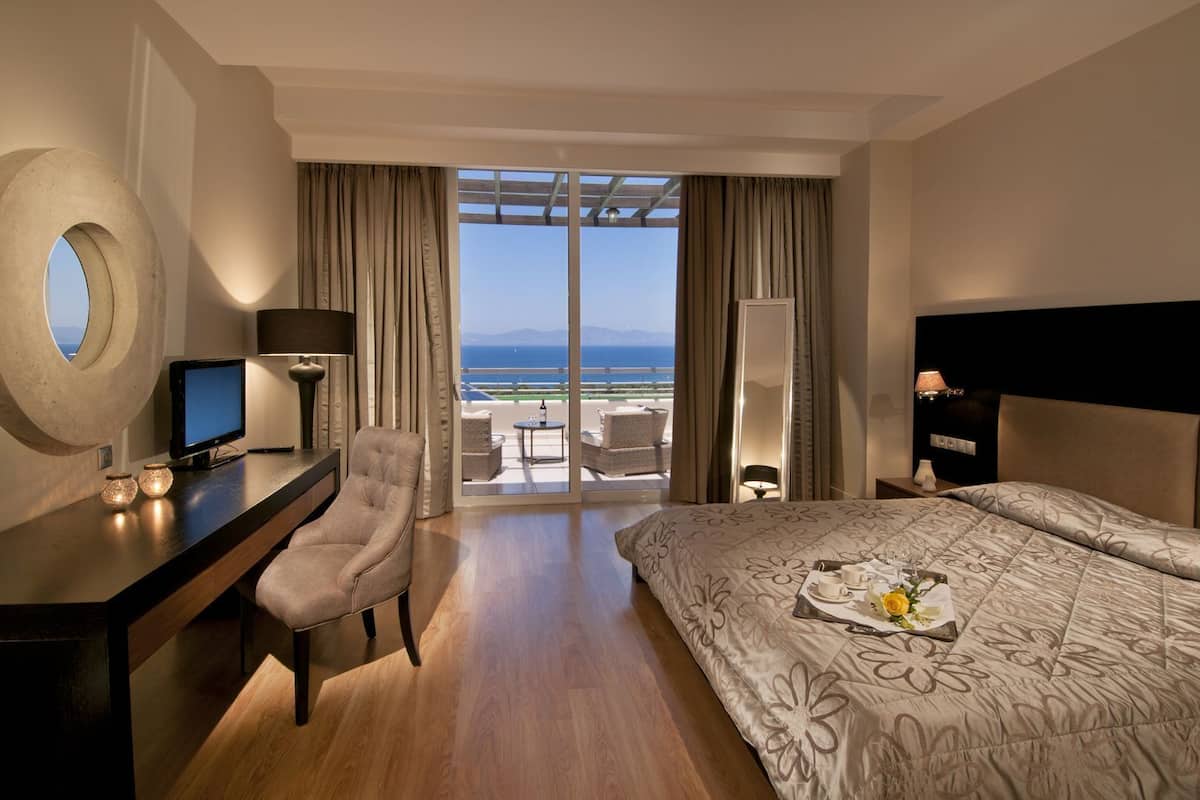 A hotel room with a bed, desk, chair, and a view of the sea.
