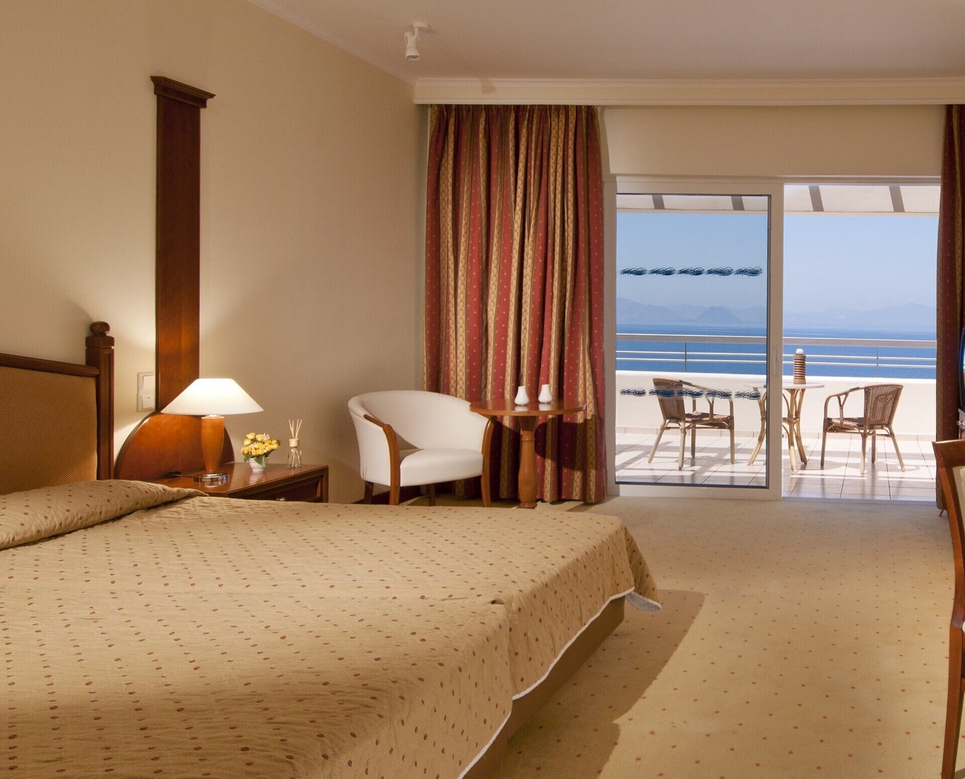 Ein Hotelzimmer mit Bett, Stuhl, Tisch, Lampe und Blick auf den Strand.