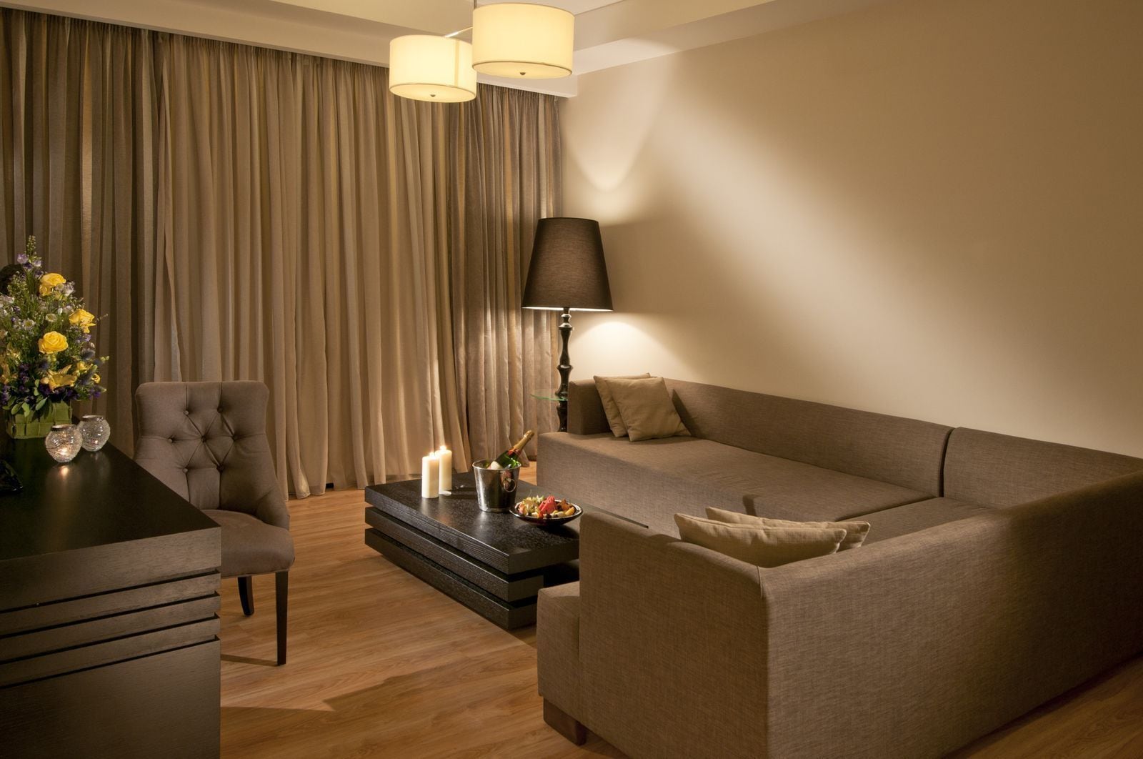 A modern living room with a sofa, armchair, and a coffee table with a bottle of champagne and candles.