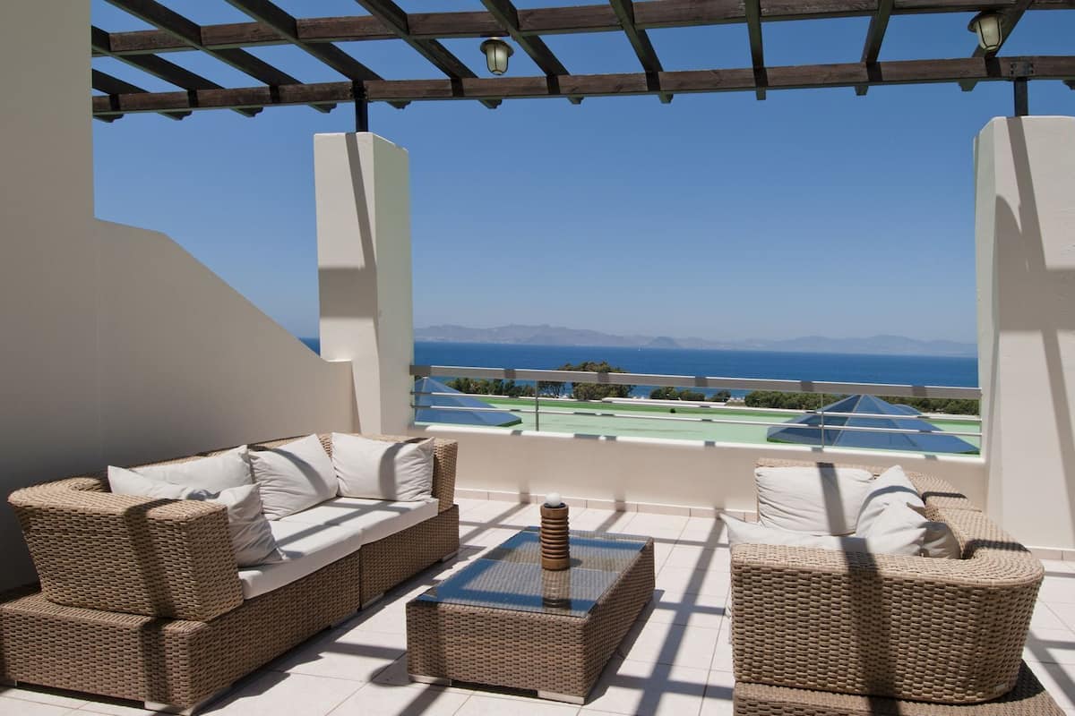 Een balkon met rieten meubilair, uitzicht op zee en een tennisbaan.