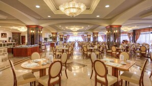 A spacious hotel dining area with multiple tables and chairs, a central bar, and a chandelier. - Kipriotis Panorama and Suites (Kos)