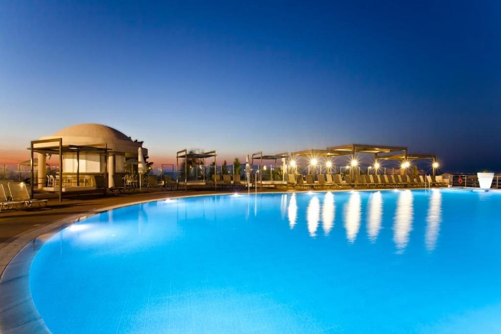 A swimming pool with lounge chairs and a pavilion at dusk.