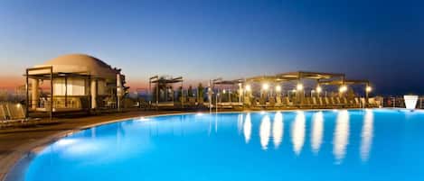 Ein Schwimmbecken mit Liegestühlen und einem Pavillon im Abenddämmerung.