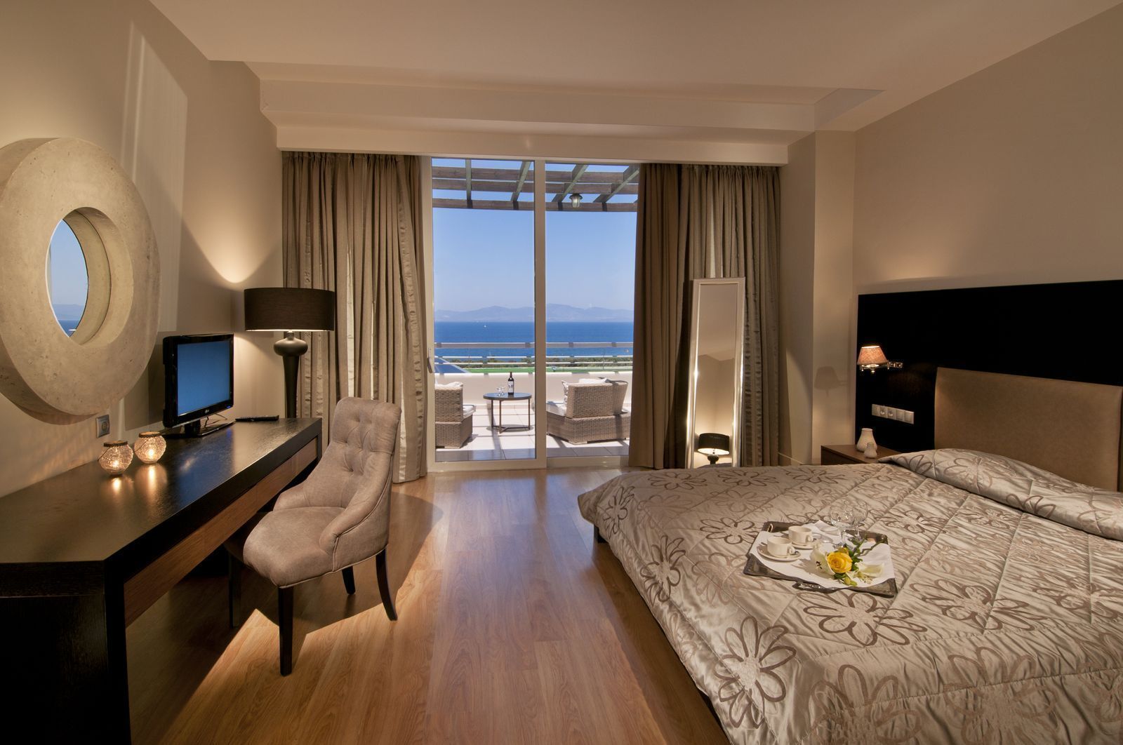 A hotel room with a bed, desk, chair, and a view of the sea.