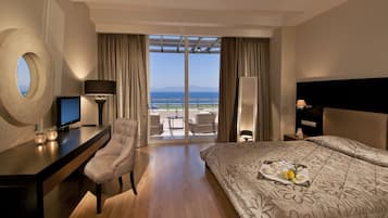 A hotel room with a bed, desk, chair, and a view of the sea.