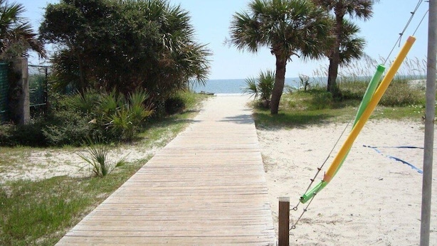 Una pasarela de madera que lleva a la playa, con palmeras y una vista despejada del océano.
