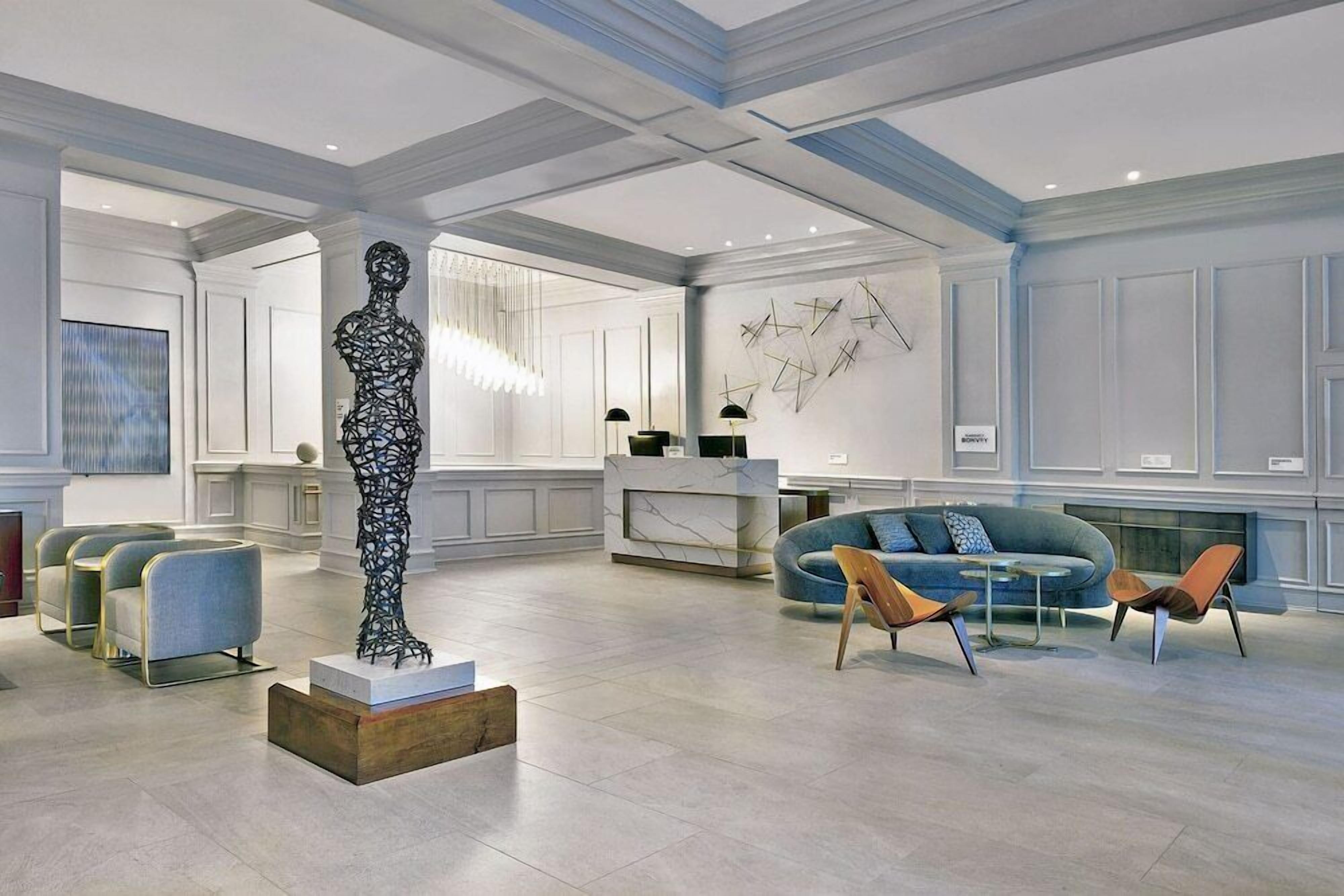 A spacious lobby with a marble reception desk, modern seating, and a large abstract sculpture.
