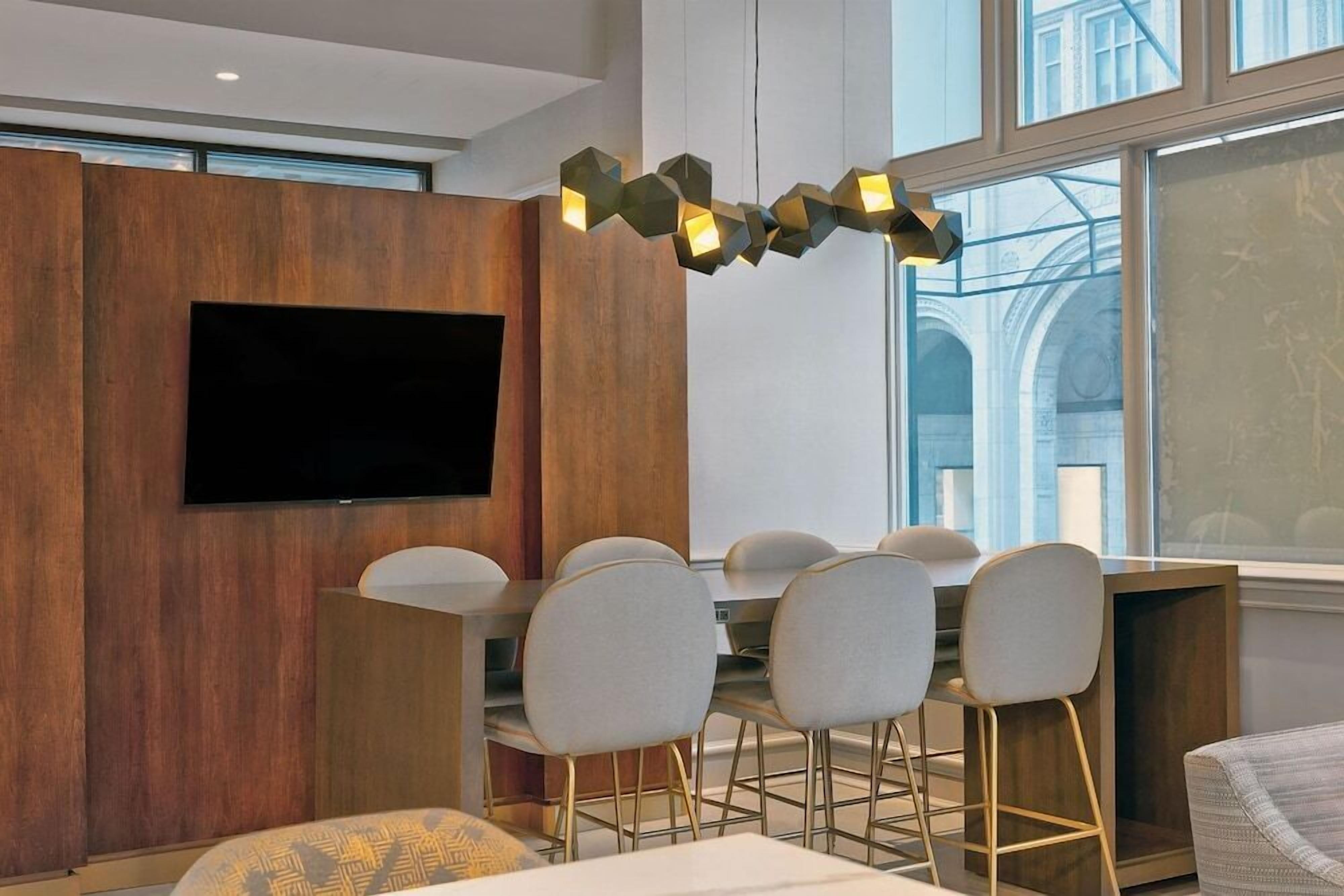 A modern dining area with a wooden accent wall, a flat-screen TV, and a unique geometric pendant light.