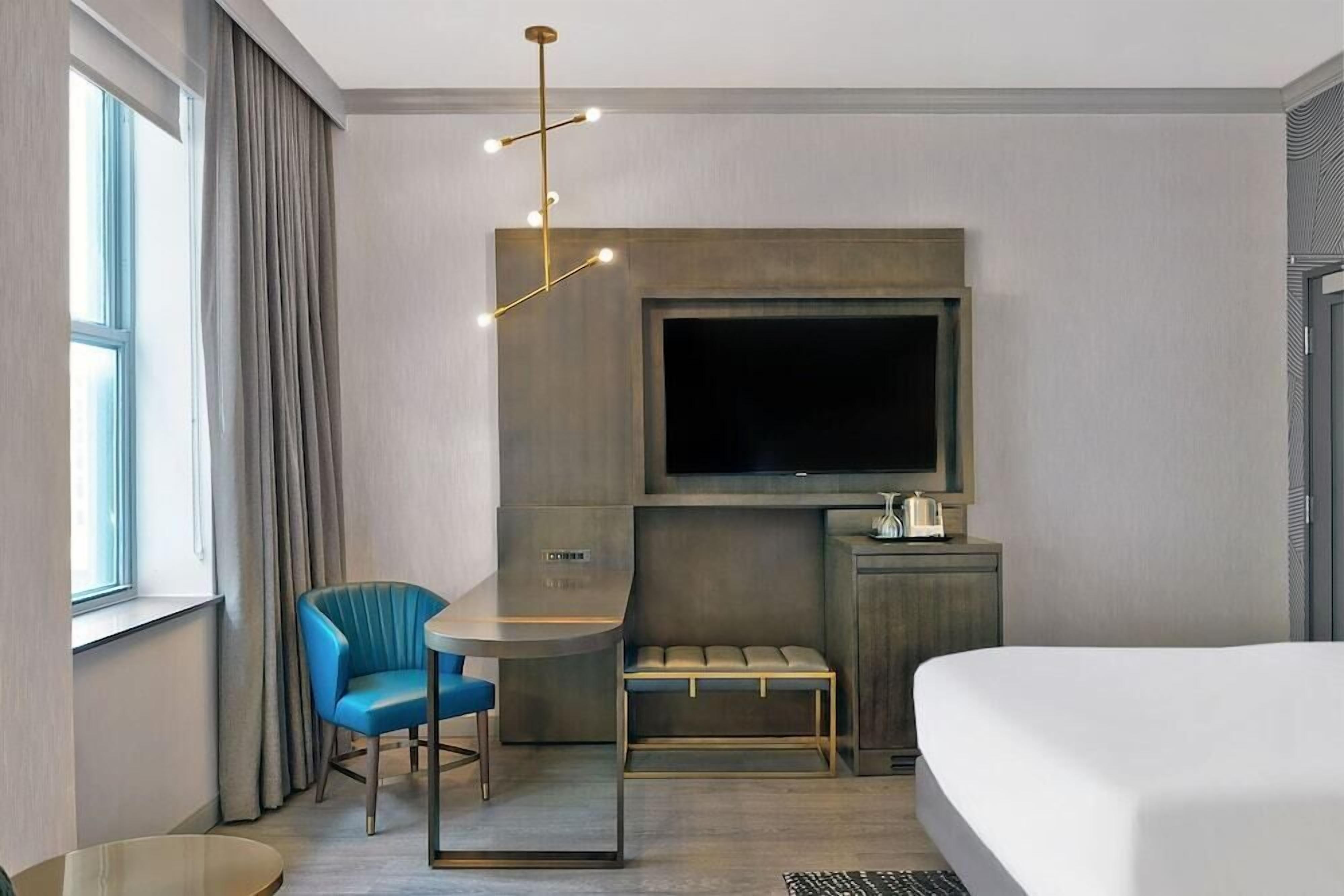 Une chambre d’hôtel moderne avec un grand lit, un téléviseur fixé au mur, une petite table avec une chaise et un banc.