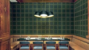 A dining area with a booth seating arrangement, a table set for four, and a green patterned wall. - Le Meridien St Louis Downtown (St. Louis)