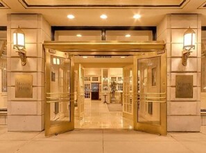 A hotel entrance with a golden gate, glass doors, and wall-mounted lights. - Le Meridien St Louis Downtown (St. Louis)