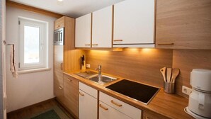 Une cuisine compacte dotée d’un four à micro-ondes encastré, d’un évier et d’armoires en bois.
