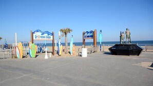 Um calçadão à beira-mar com pranchas de surf, uma placa indicando 'Harris's Moyers & Storage' e uma torre de salva-vidas.