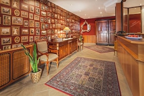 Una hall con una parete di quadri incorniciati, una scrivania della reception, un tappeto grande e decorativo e un bancone in legno.