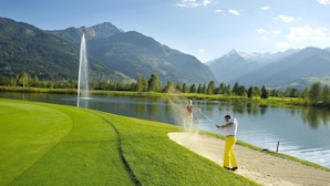 Un campo de golf con una fuente, un lago y montañas al fondo.
