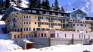 A multi-story hotel with a snow-covered exterior, surrounded by trees and mountains. - Schuetz (Untertauern)