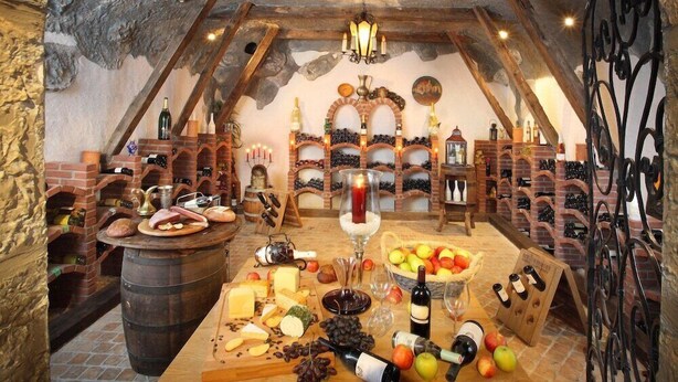 An underground cellar with wine racks, a cheese and fruit display, and a rustic wooden table. - Schuetz (Untertauern)