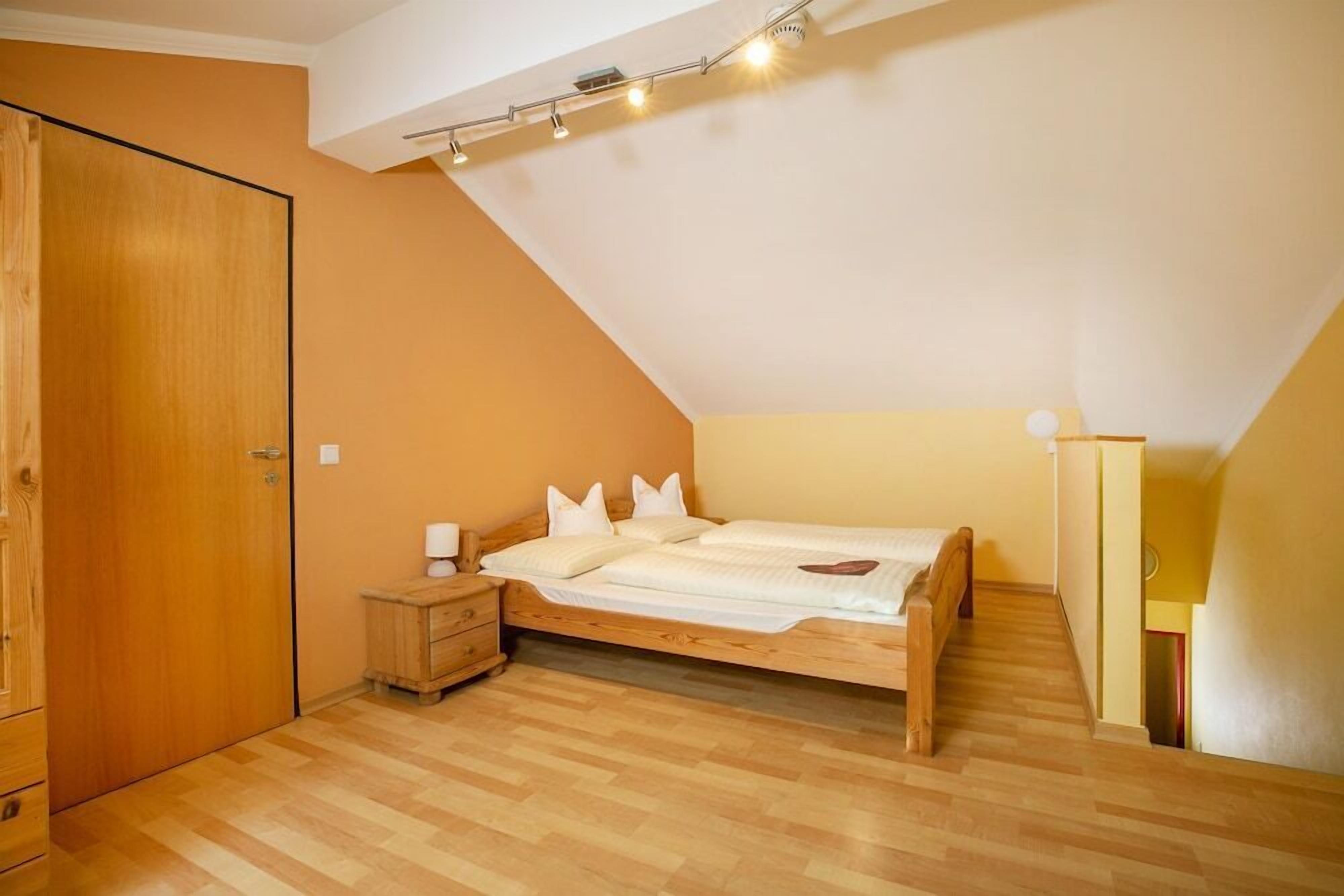 A bedroom with a wooden bed, a nightstand, a wardrobe, and a sloped ceiling with track lighting.
