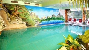 An indoor swimming pool with a mural of a mountainous landscape, lounge chairs, and tropical plants. - Schuetz (Untertauern)