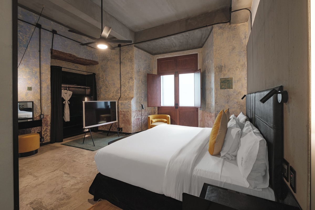 A hotel room with a large bed, a flat-screen TV, a wooden wardrobe, and a window with curtains.