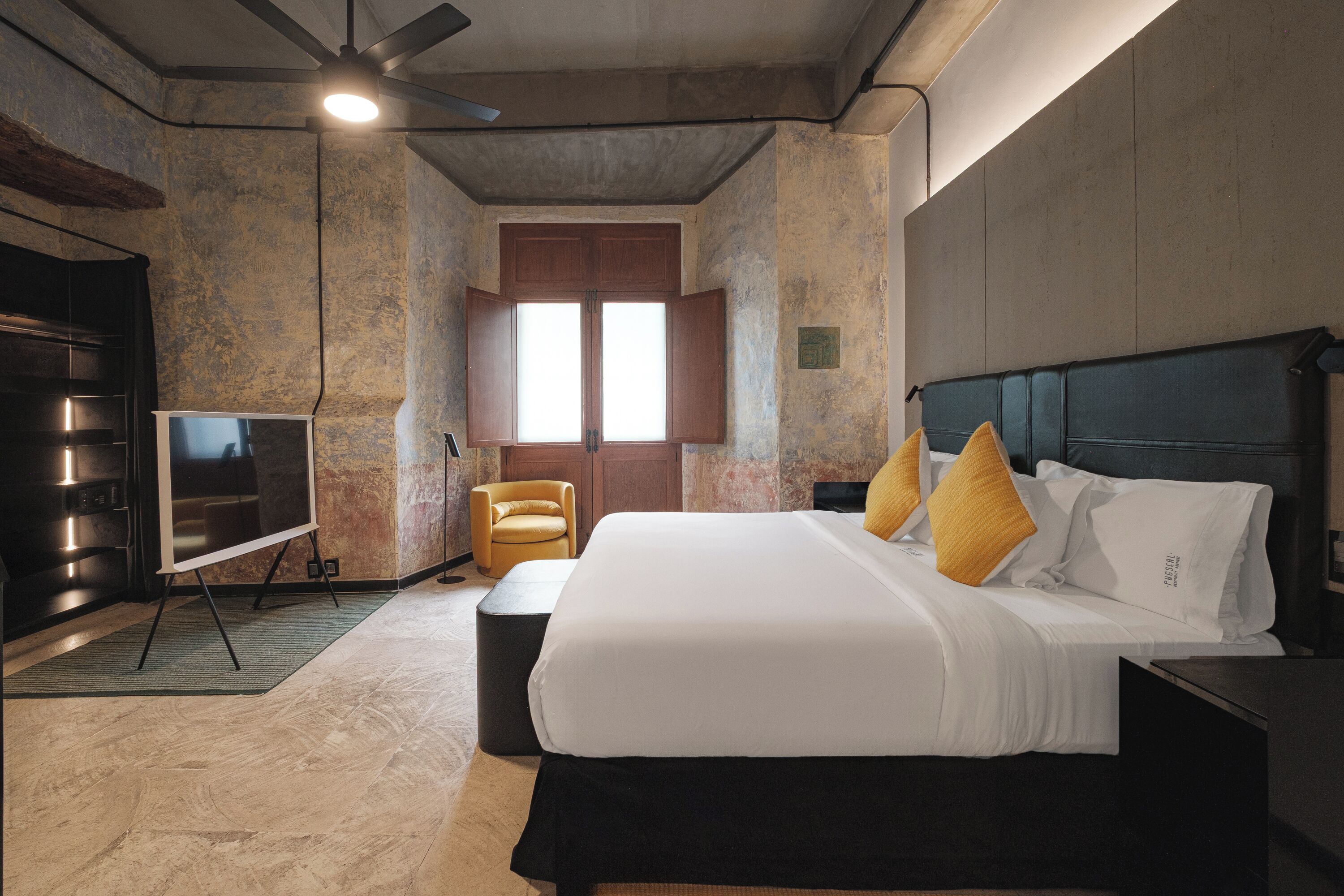 A modern hotel room with a large bed, a flat-screen TV, a ceiling fan, and a wooden wardrobe.