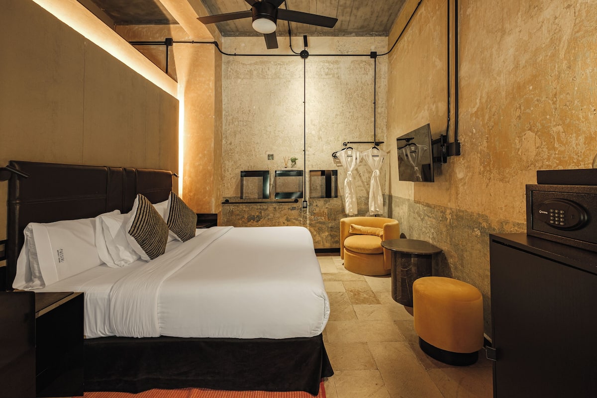 A modern hotel room with a large bed, a small stool, a microwave, and a ceiling fan.