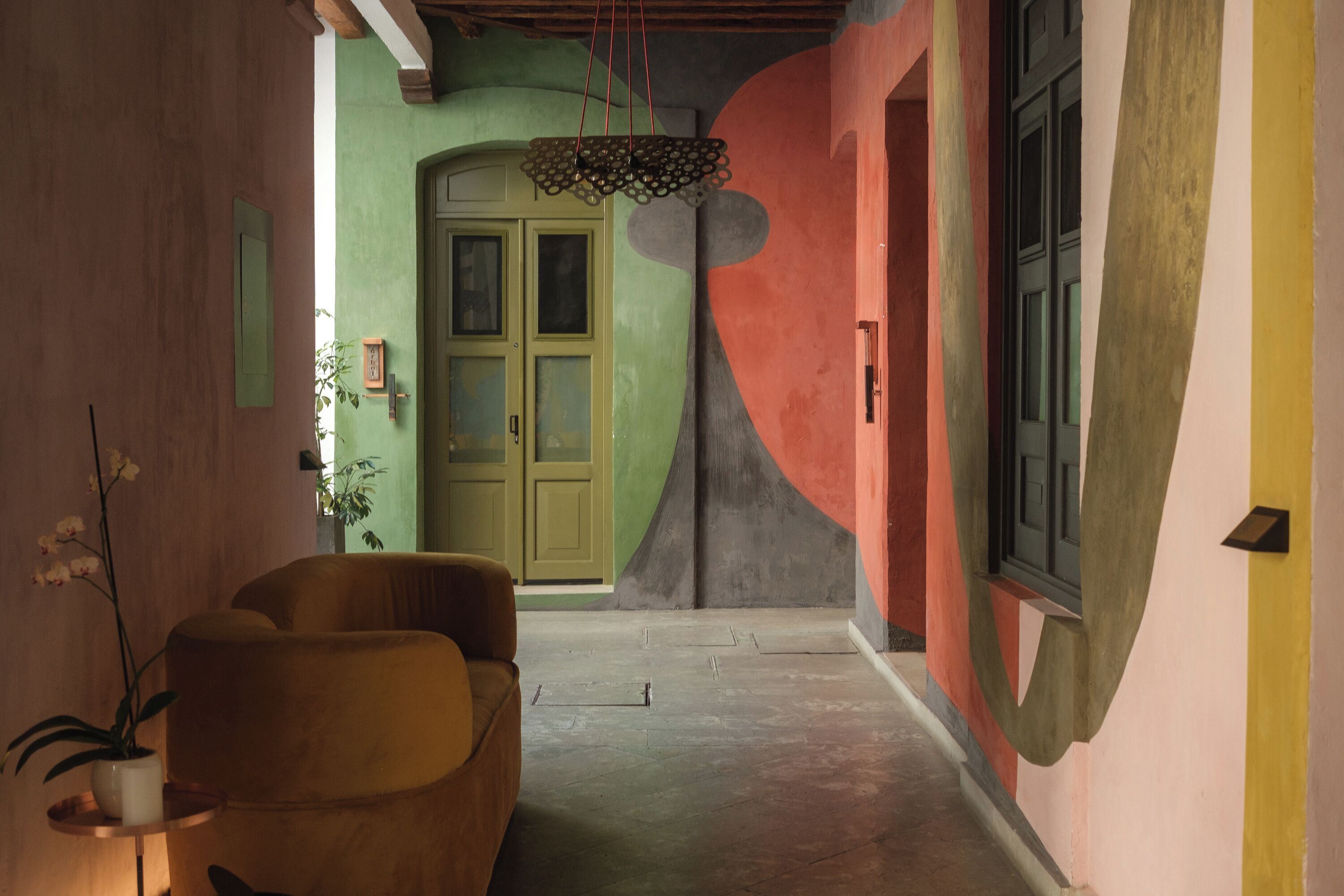 A hallway with a green door, a yellow armchair, and a hanging light fixture.