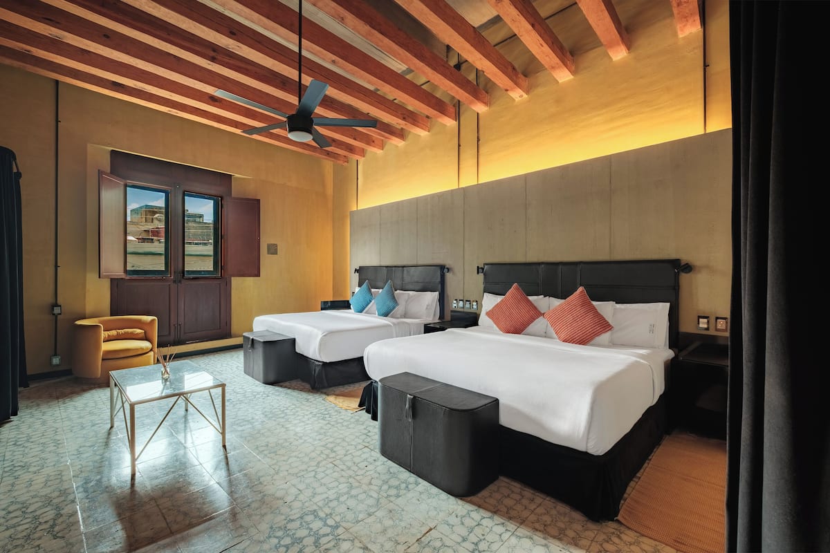 A hotel room with two beds, a sofa, a small table, and a ceiling fan.
